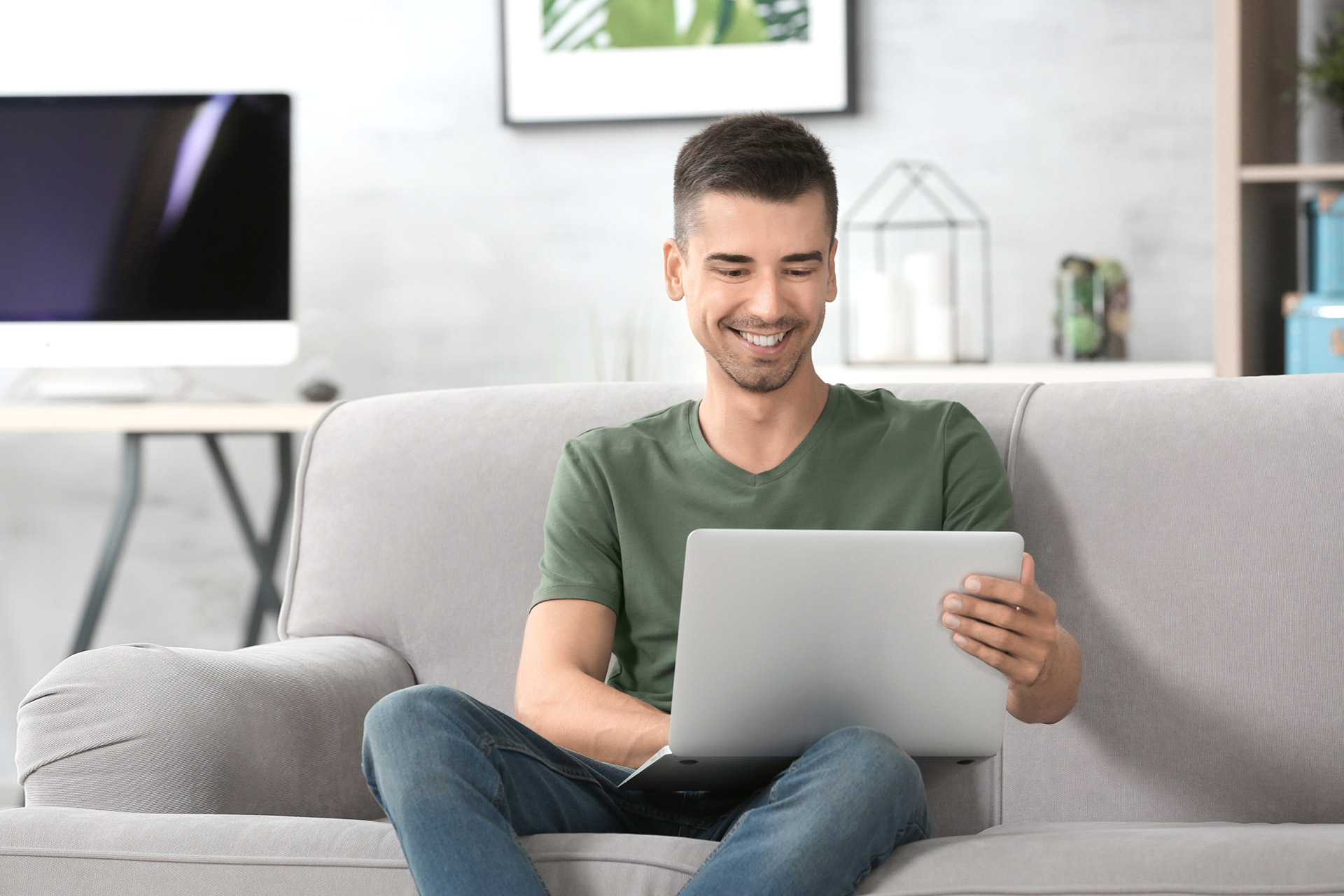 Homem sentado no sofá usando o laptop no colo